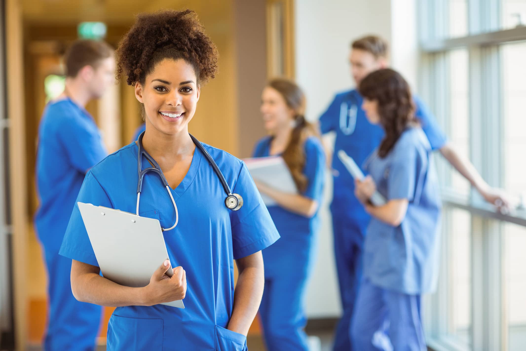 Smiling female nurse in blue scrubs with team in background