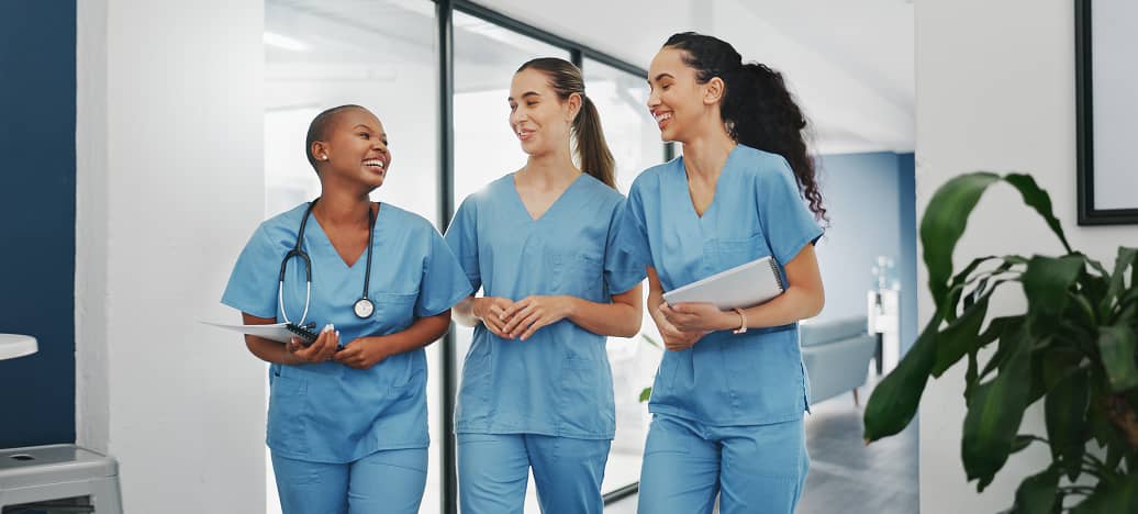 Three nurses in blue scrubs laughing together